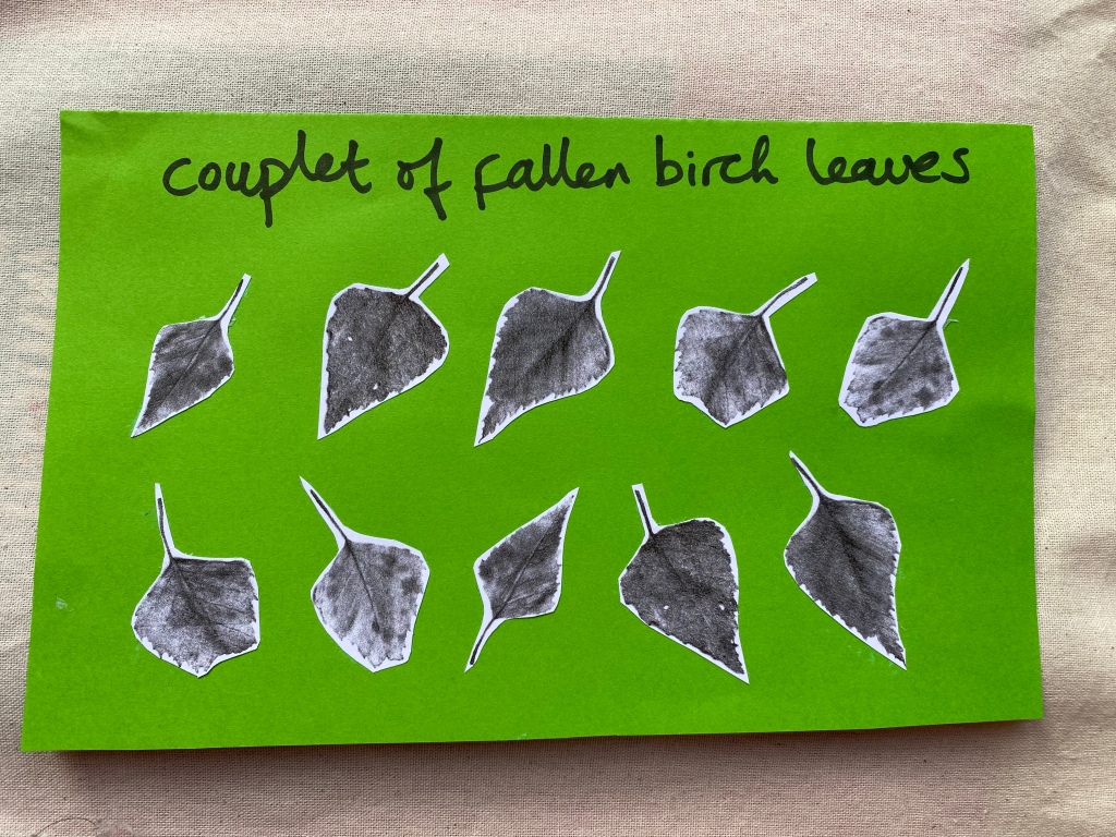 Paper cut-outs of leaves arranged on green paper in two lines as in a poem. Handwritten text reads "couplet of fallen birch leaves".