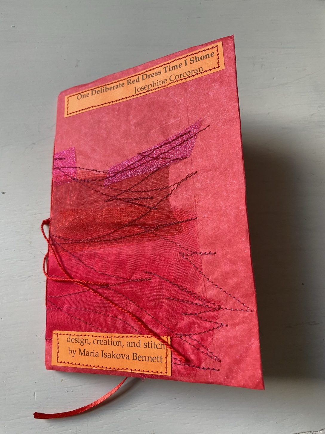 Close up of handstitched red-covered pamphlet 'One Deliberate Red Dress Time I Shone' by Josephine Corcoran. Text reads 'design, creation, and stitch by Maria Isakova Bennett