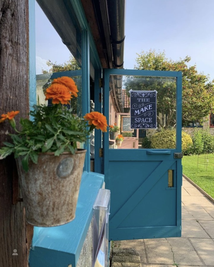 A pot of marigolds and an open blue door at The Make Space, Bradford-on-Avon