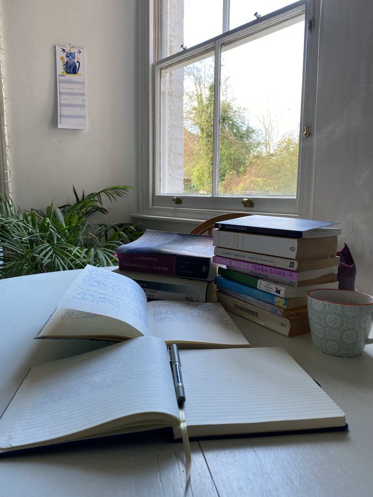 An open notebook on a table by a sash window on which can be seen a small stack of books